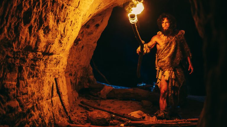 Primeval,Caveman,Wearing,Animal,Skin,Exploring,Cave,At,Night,,Holding