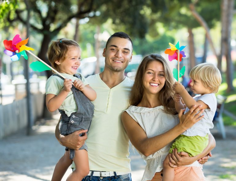 Happy,Little,Girls,With,Windmills,Sitting,On,Parent's,Arms,Outdoor.