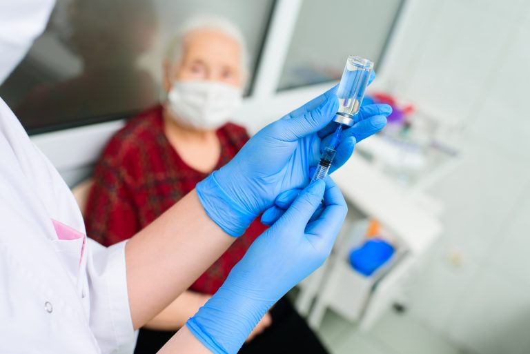 A,Doctor,Wearing,Rubber,Gloves,Prepares,To,Inject,An,Elderly