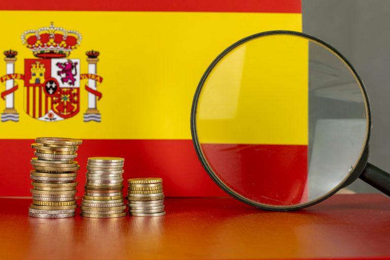 Magnifying,Glass,And,Coins,In,Front,Of,Spain,Flag,,Country