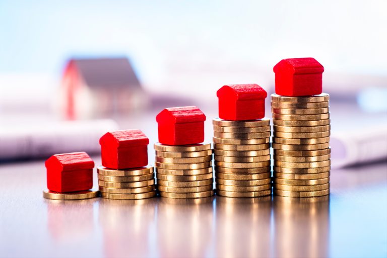 Small,Red,Houses,Standing,On,Stacks,Of,Coins,With,Blueprints