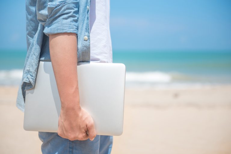Man,Hand,Holding,Laptop,At,The,Beach,,Working,Outdoor,In