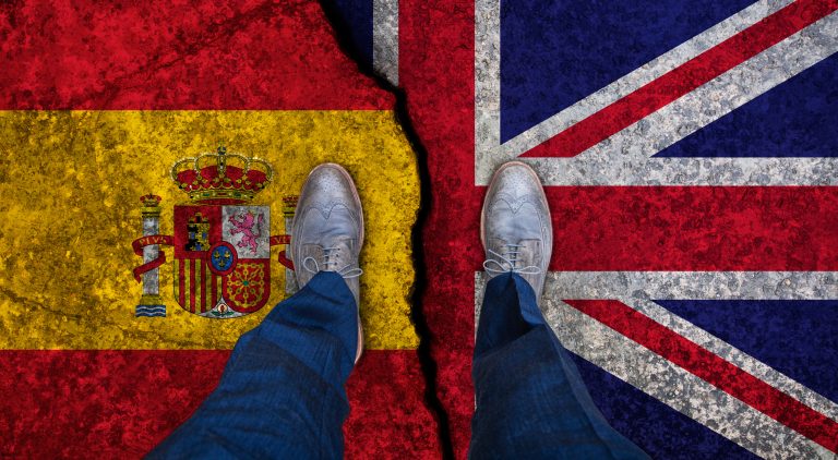 Business,Man,Stands,On,Cracked,Flag,Of,Uk,And,Spain.