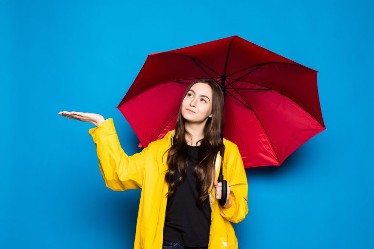 Young,Woman,Wearing,Rain,Coat,Holding,Colorful,Umbrella,Over,Blue