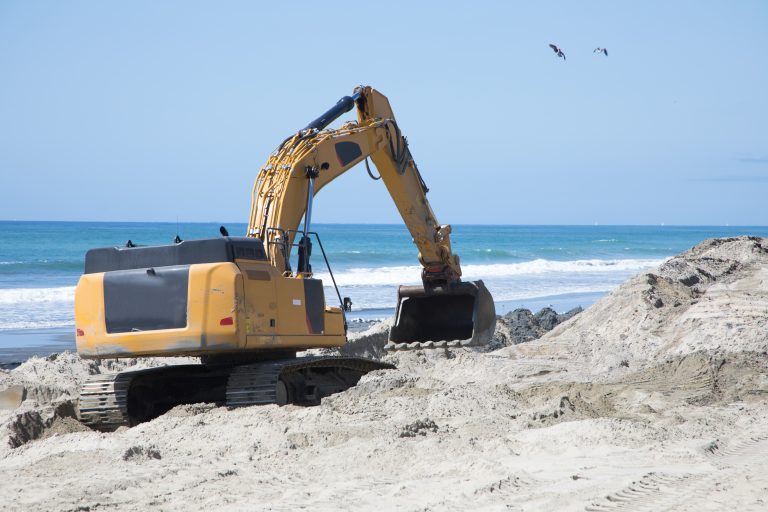 Construction,Excavator,Working,On,Beach,Sand,Defense,With,Ocean,In