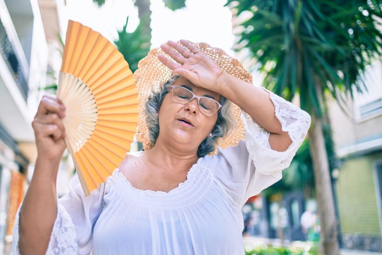 Middle,Age,Woman,With,Grey,Hair,Using,Handfan,On,A