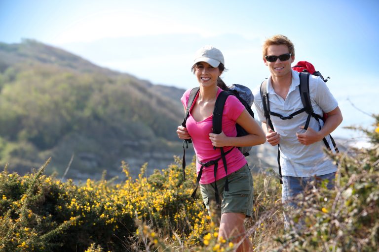 Couple,Of,Hikers,In,Country,Field,By,The,Ocean