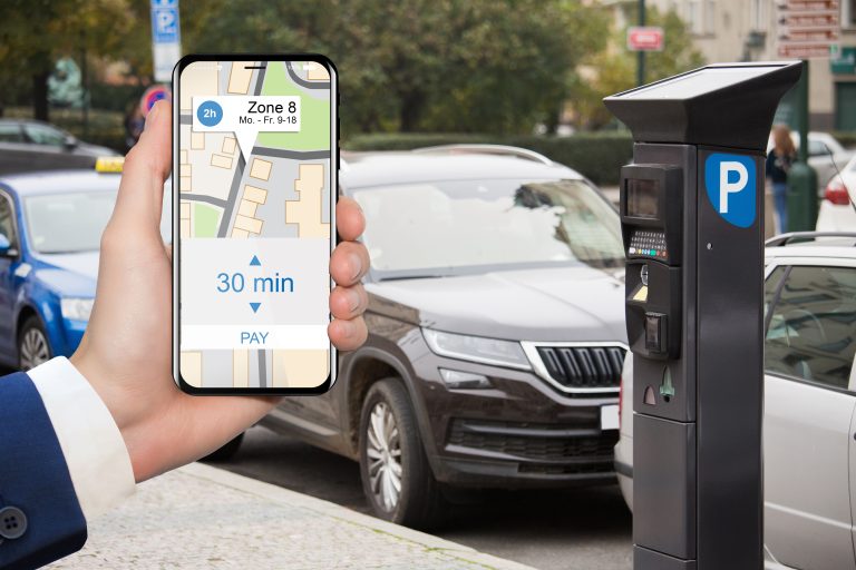 Hand,With,Phone,On,The,Background,Of,The,Parking,Machine.