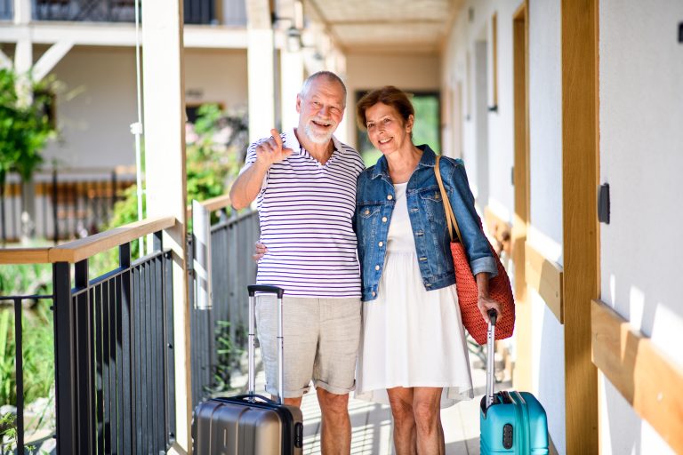 Senior,Couple,With,Luggage,Outside,Apartment,On,Holiday.