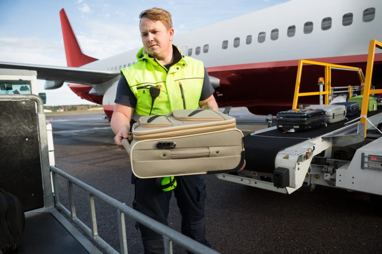 Worker,Placing,Luggage,In,Trailer,Against,Airplane