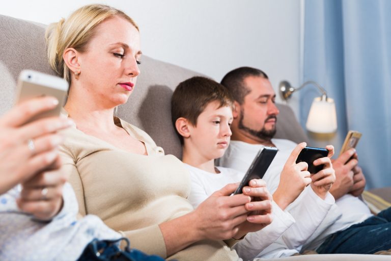 Young,Parents,With,Son,Using,Mobile,Gadgets,On,Sofa,At