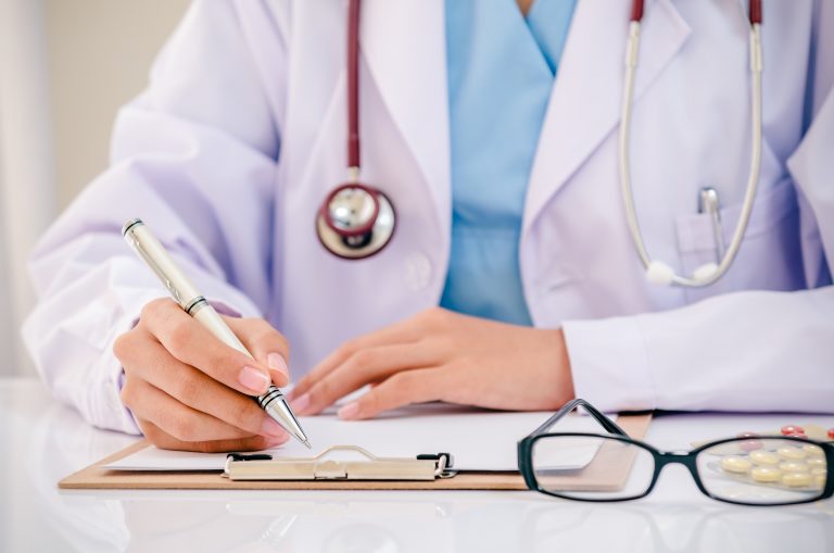 Doctor,Writing,Record,On,Folder,While,Holding,Medicine,In,Office