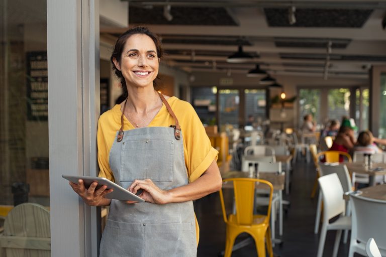 Portrait,Of,A,Happy,Waitress,Standing,At,Restaurant,Entrance,Holding