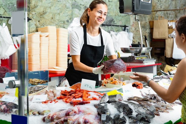 Polite,Glad,Cheerful,Positive,Female,Fishmonger,Standing,Behind,Counter,Of