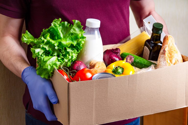 Volunteer,In,Gloves,Holding,Food,In,A,Donation,Cardboard,Box