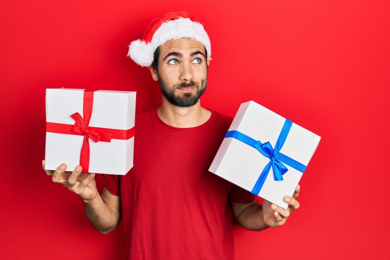 Young,Hispanic,Man,Wearing,Christmas,Hat,And,Holding,Gifts,Smiling