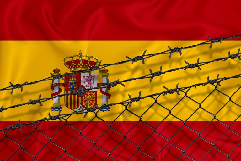 Developing,Spain,Flag,,Mesh,Fence,And,Barbed,Wire.,Concept,Of