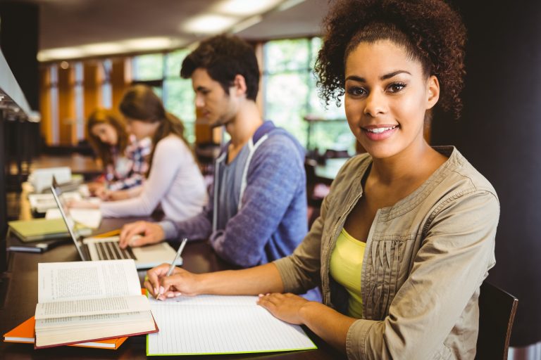 Student,Looking,At,Camera,While,Studying,With,Classmates,In,Library