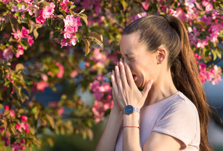 Young,Pretty,Woman,Sneezing,In,Front,Of,Blooming,Tree.,Spring