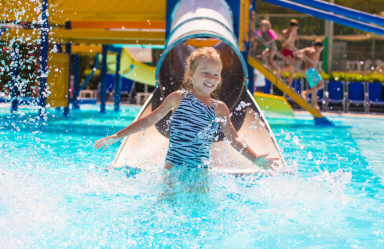 Little,Girl,On,Water,Slide,At,Aquapark,During,Summer,Holiday