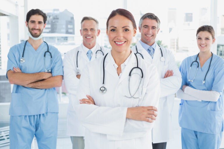 Smiling,Doctor,With,Fellow,Doctors,Standing,Behind,Her
