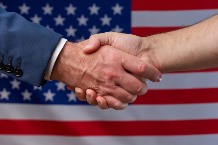 Two,Men,Shaking,Hands,With,The,United,States,Flag,In
