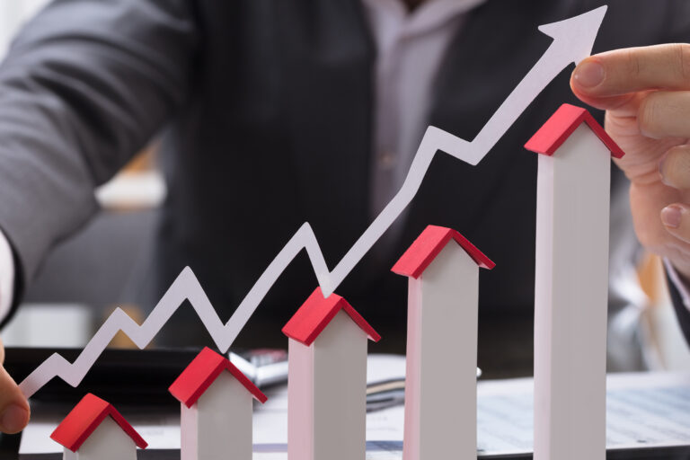 Businessman,Holding,Paper,Graph,Over,The,Increasing,House,Miniature