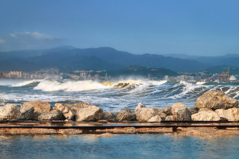 Stormy,Sea,With,Urban,Landscape,And,Mountains,On,The,Background.