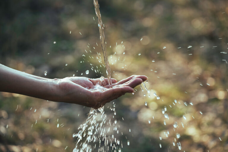 Water,Flow,To,Hand,In,The,Garden,On,Nature,Background.