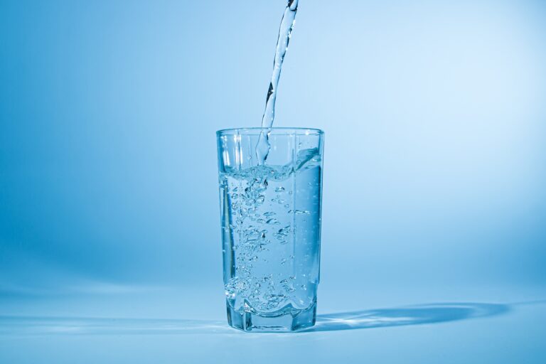 Water,Pours,Into,A,Glass,On,A,Blue,Background.,Clean