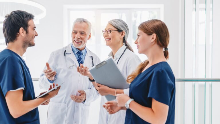 Smiling,Group,Of,Medical,Staff,Discussing,In,Clinic,Corridor,,Giving