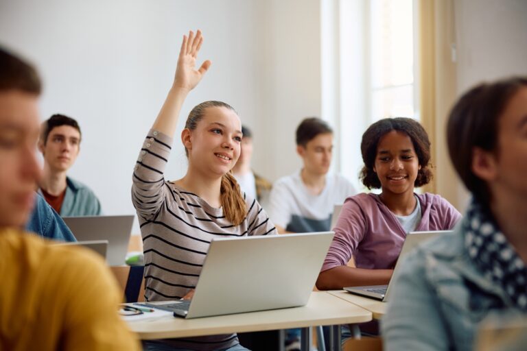 Smiling,High,School,Student,Raising,Her,Arm,During,Computer,Class
