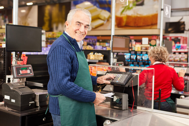 Friendly,Cashier,With,Green,Apron,At,The,Cash,Register,In