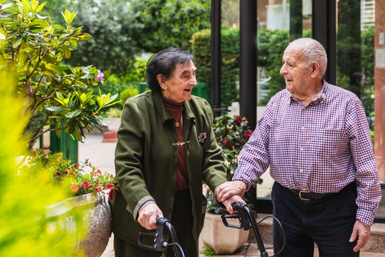 Happy,Elderly,Couple,Using,Walkers,And,Chatting,In,The,Garden