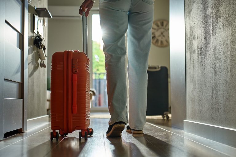Low-angle,View,Of,Traveler,Walking,Towards,Door,With,Rolling,Luggage.